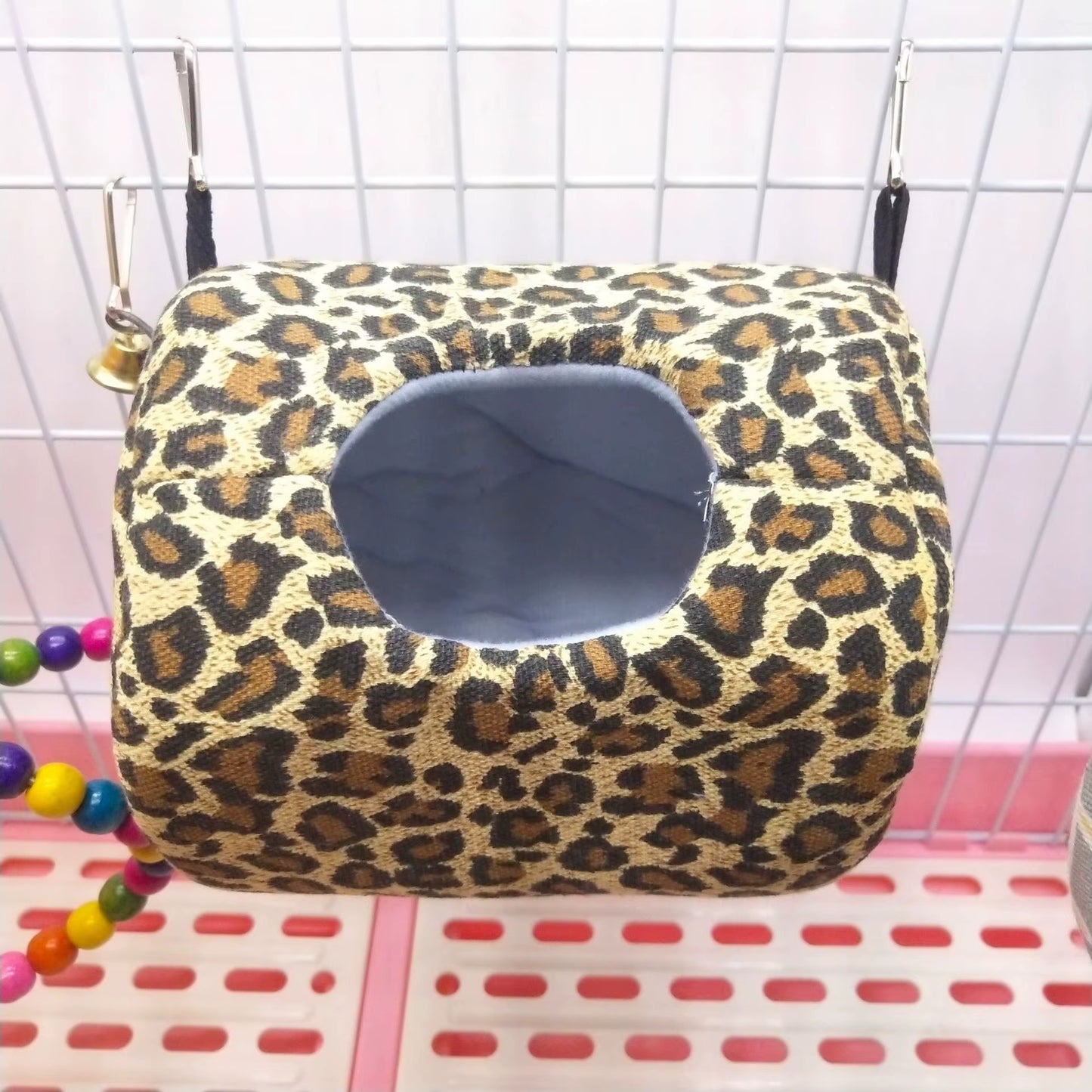 Leopard print canvas hammock bed hanging inside a small pet wire cage by two black straps